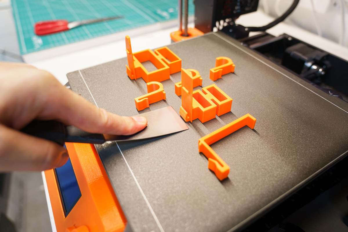 A hand removing an orange 3D printed part from a print bed