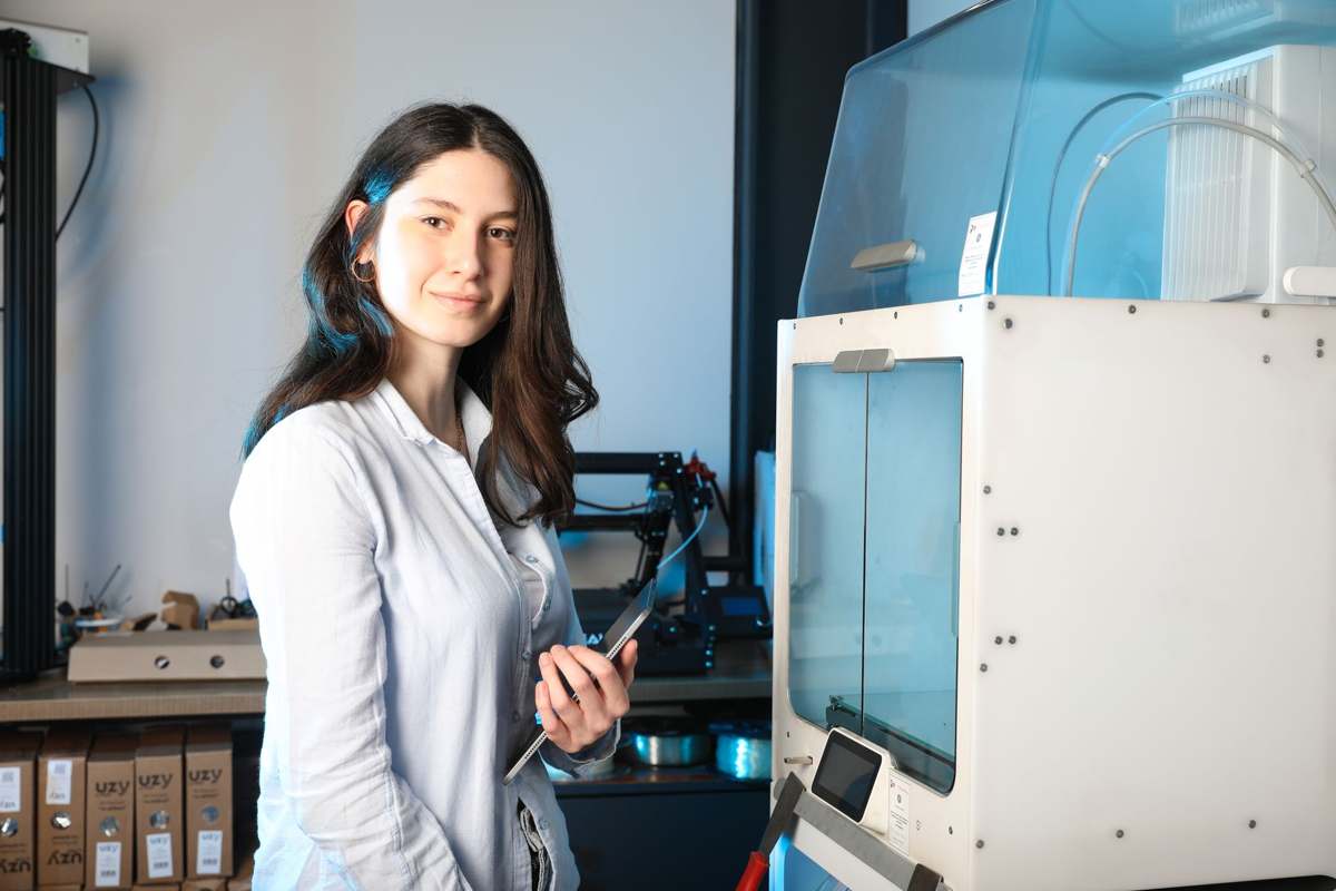 An engineer with a tablet standing beside additive manufacturing equipment