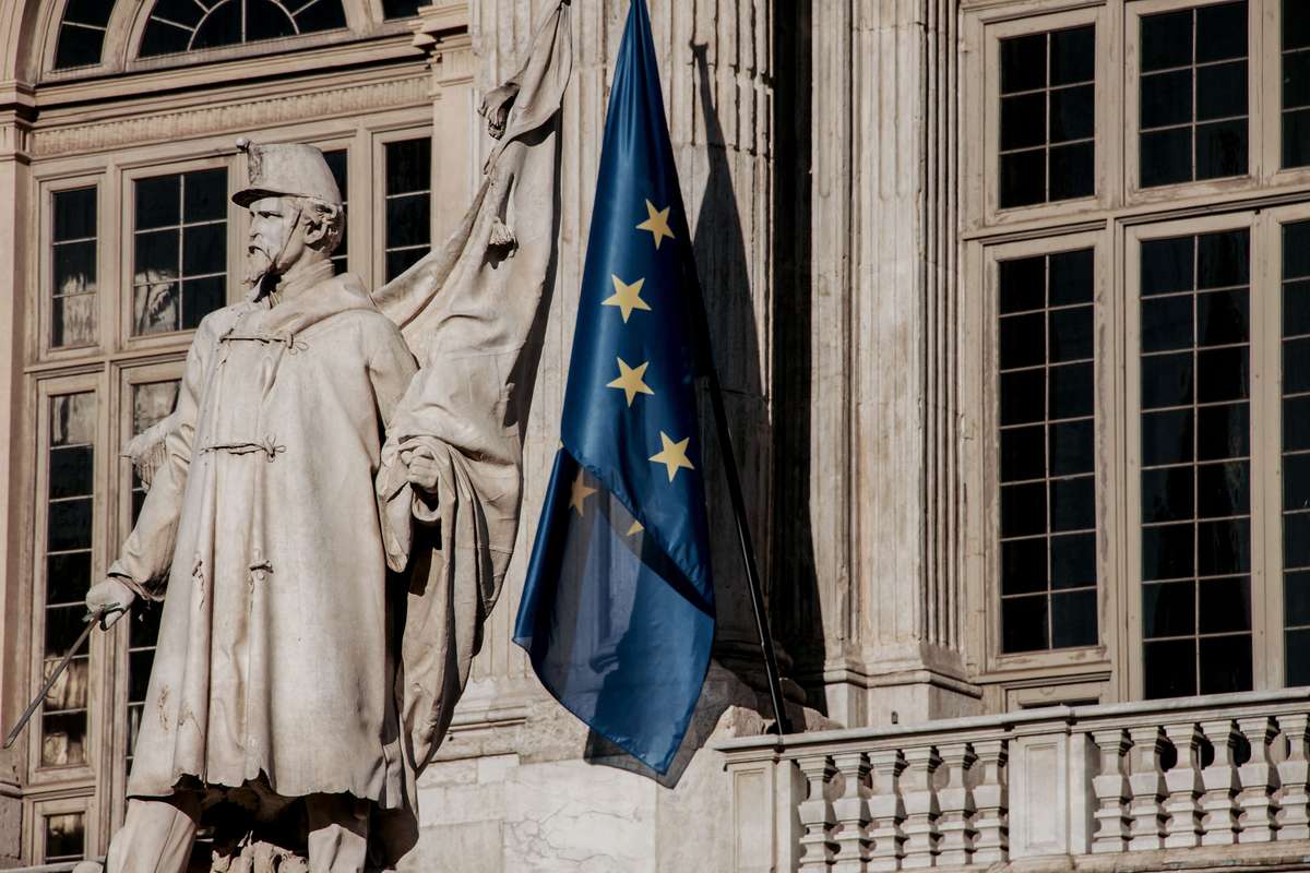 A European Union flag waving beside a statue on a historic stone facade