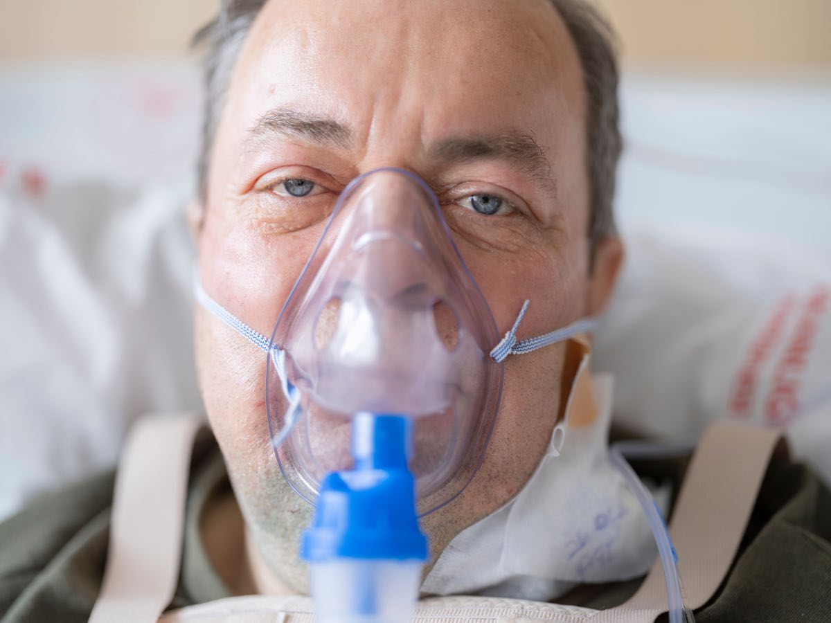 Close-up of a man in a hospital bed wearing an oxygen mask, highlighting healthcare needs