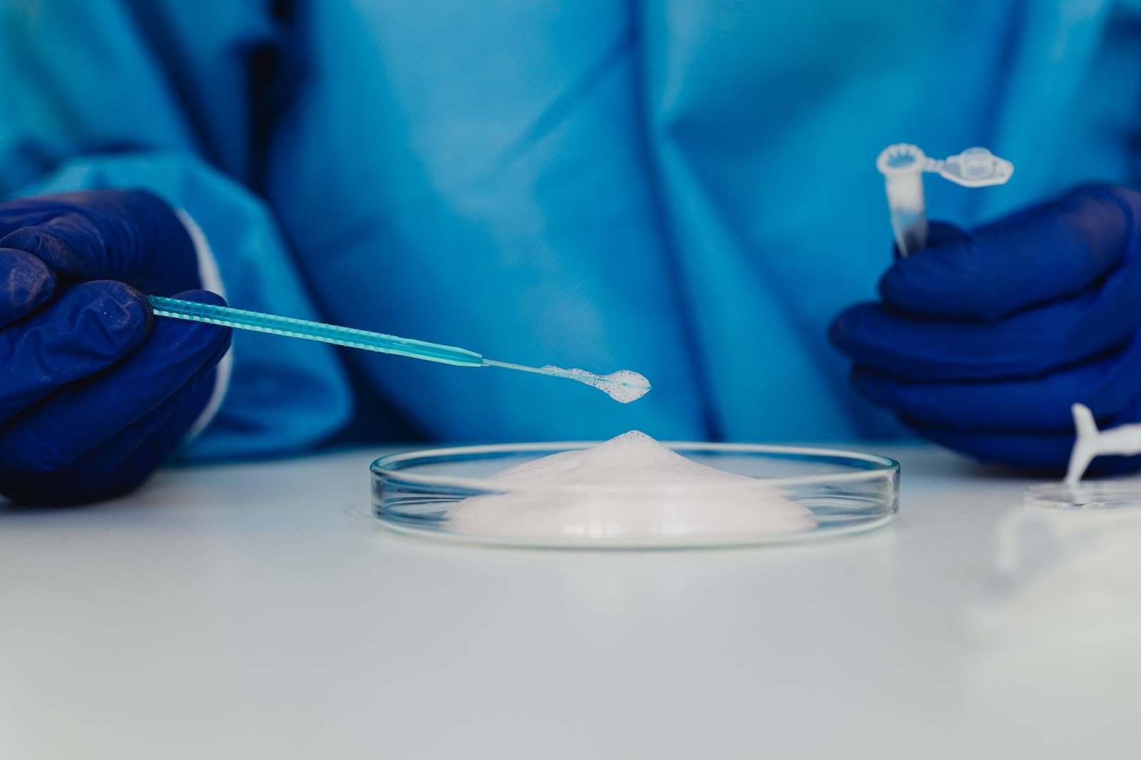 A gloved scientist working with a material sample in a petri dish