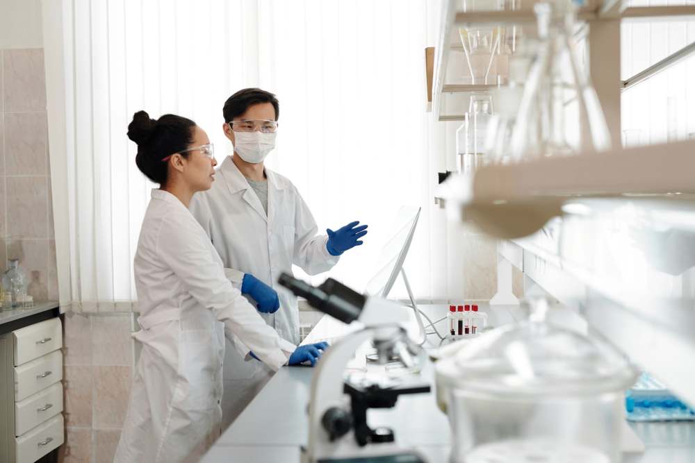 Two scientists in safety glasses discussing work in a laboratory