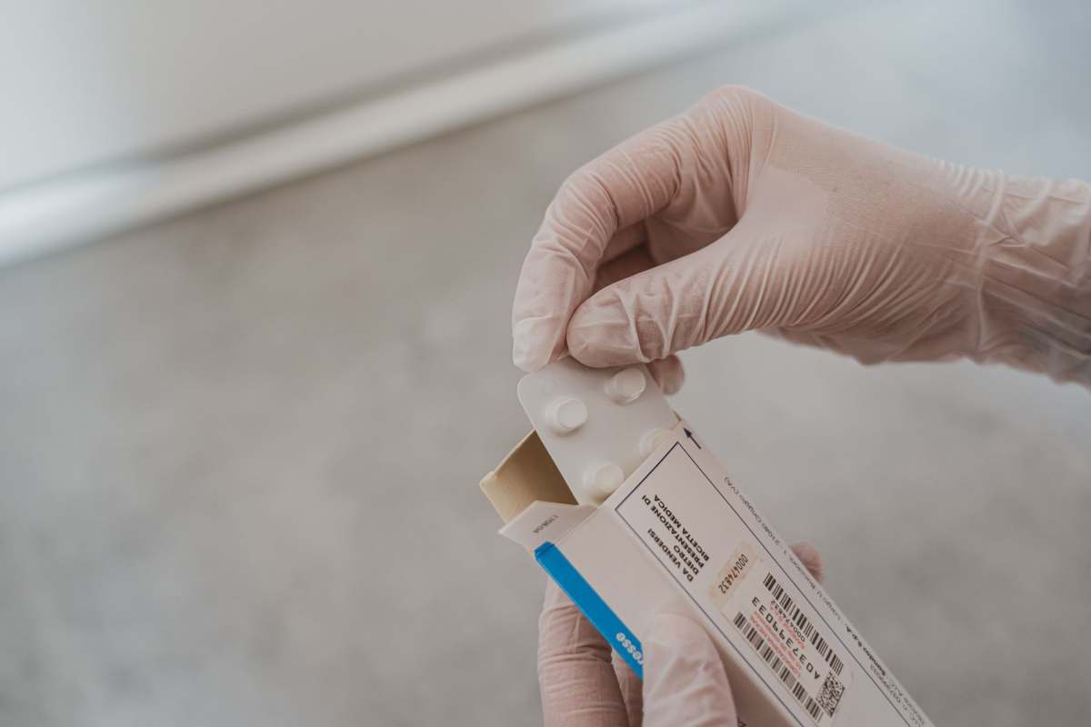 A gloved hand selecting a medicine package in a pharmacy setting