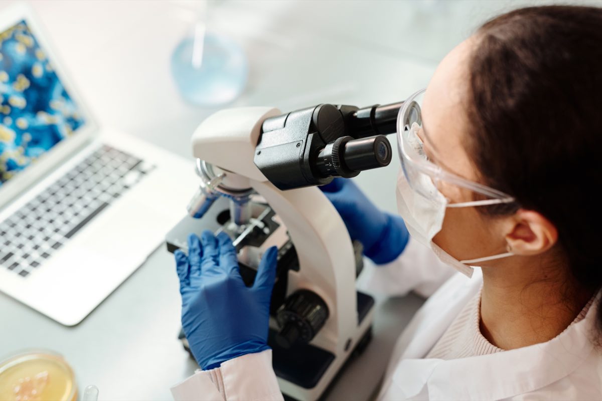 A scientist in protective gear examining samples under a microscope