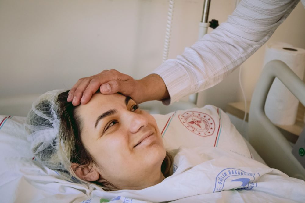A patient resting in a hospital bed with a supportive hand on their forehead