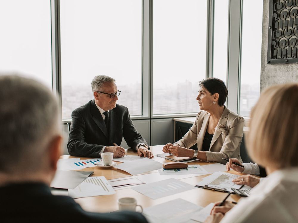 Senior leaders in a strategy session at a boardroom table, reviewing program data by a skyline window