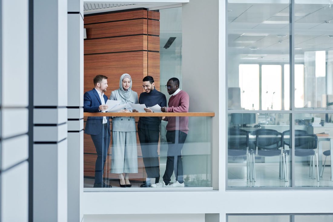 An embedded consulting team talking through a program on a glass-walled office mezzanine