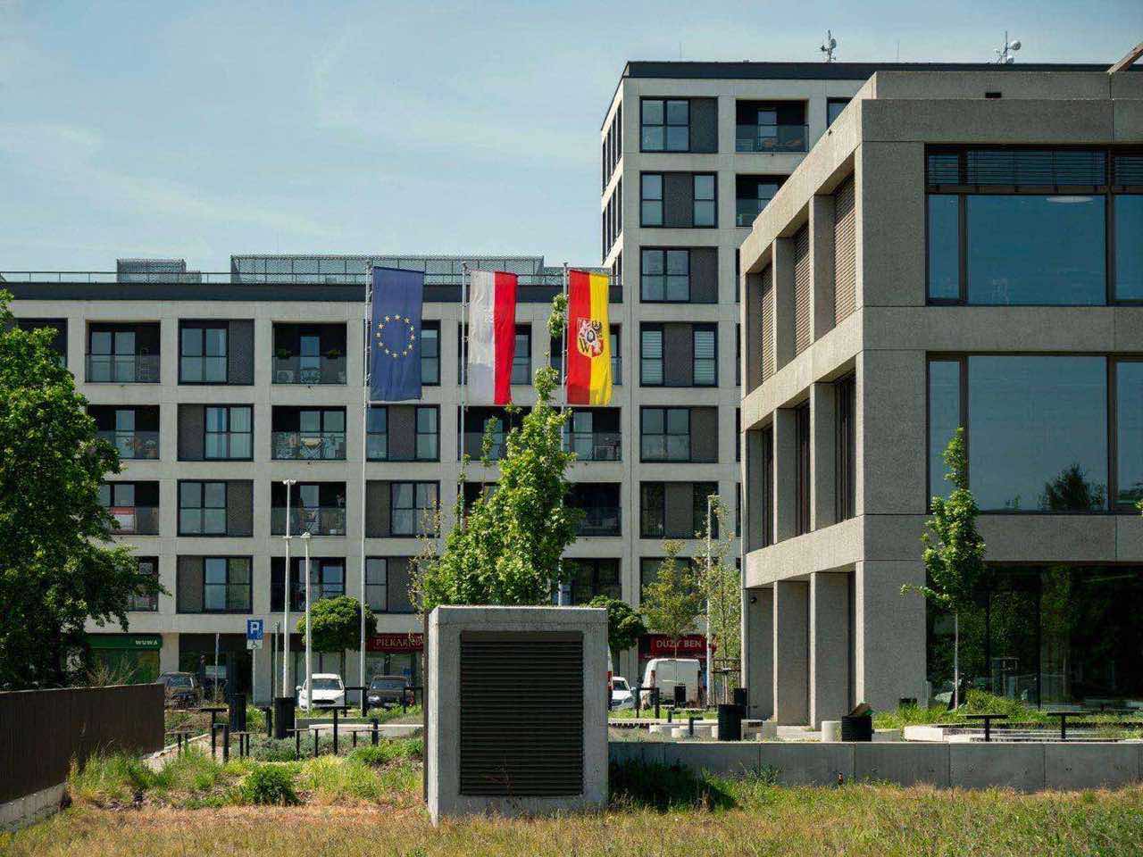 A modern European building flying the EU flag alongside a national flag