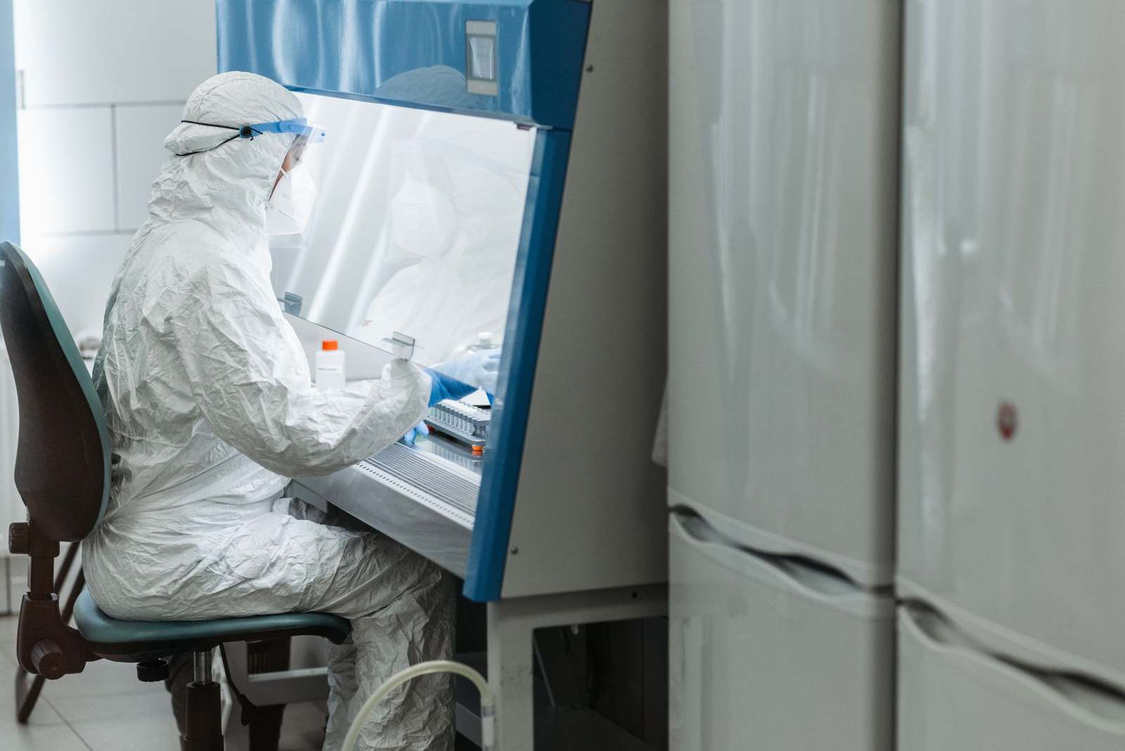 A gowned scientist working at a biosafety cabinet in a cell processing laboratory