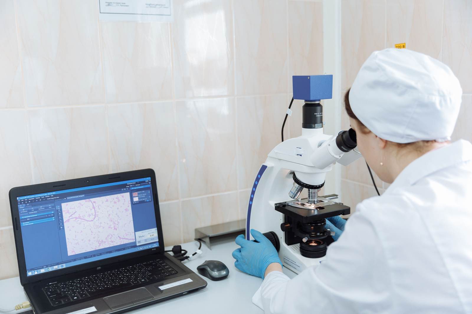 A scientist using a microscope and laptop in a laboratory