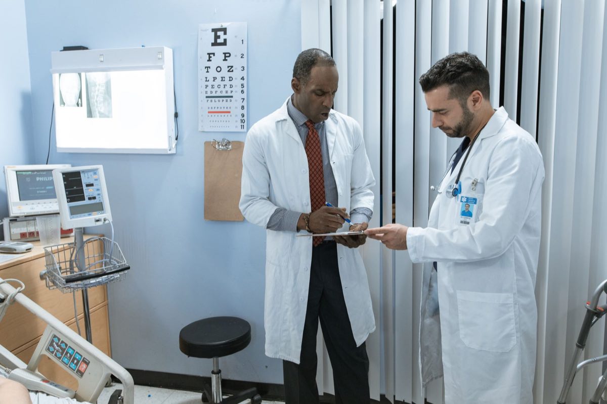 Two doctors in lab coats discussing a patient's chart in a hospital room