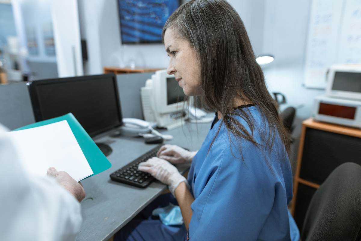 A nurse in scrubs typing at a medical workstation keyboard