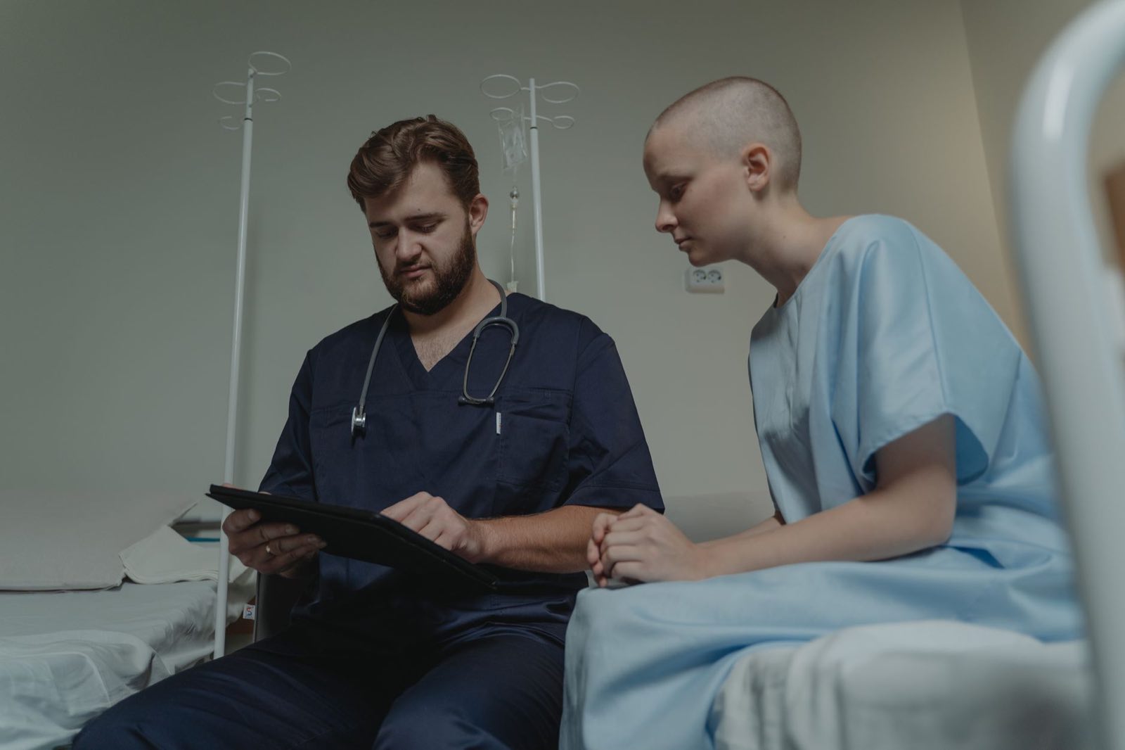 A doctor reviews information on a tablet with a patient at the bedside