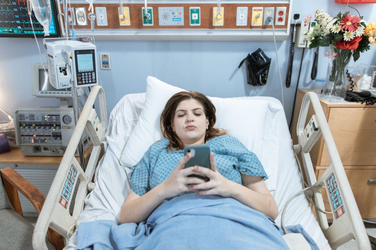 A patient in a hospital bed using a phone, surrounded by connected equipment