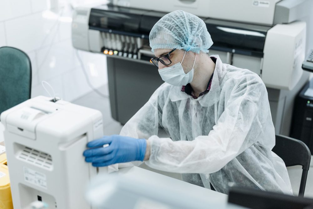 A technician in protective gear working with laboratory equipment
