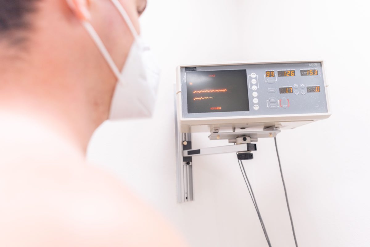 A masked patient in a clinic being monitored by an electronic device