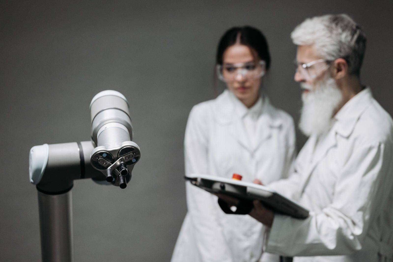 Two researchers in lab coats evaluating a collaborative robotic arm
