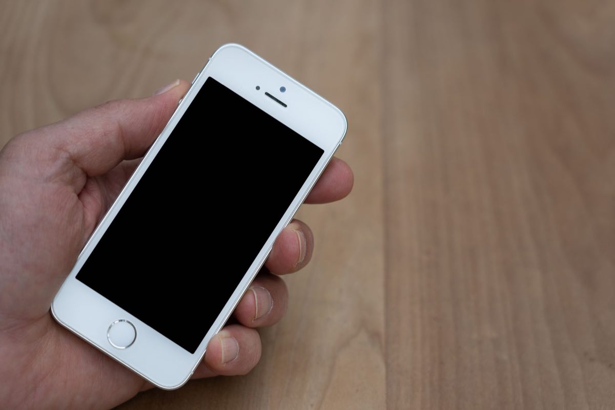 A person holding a smartphone with a blank screen over a wooden table