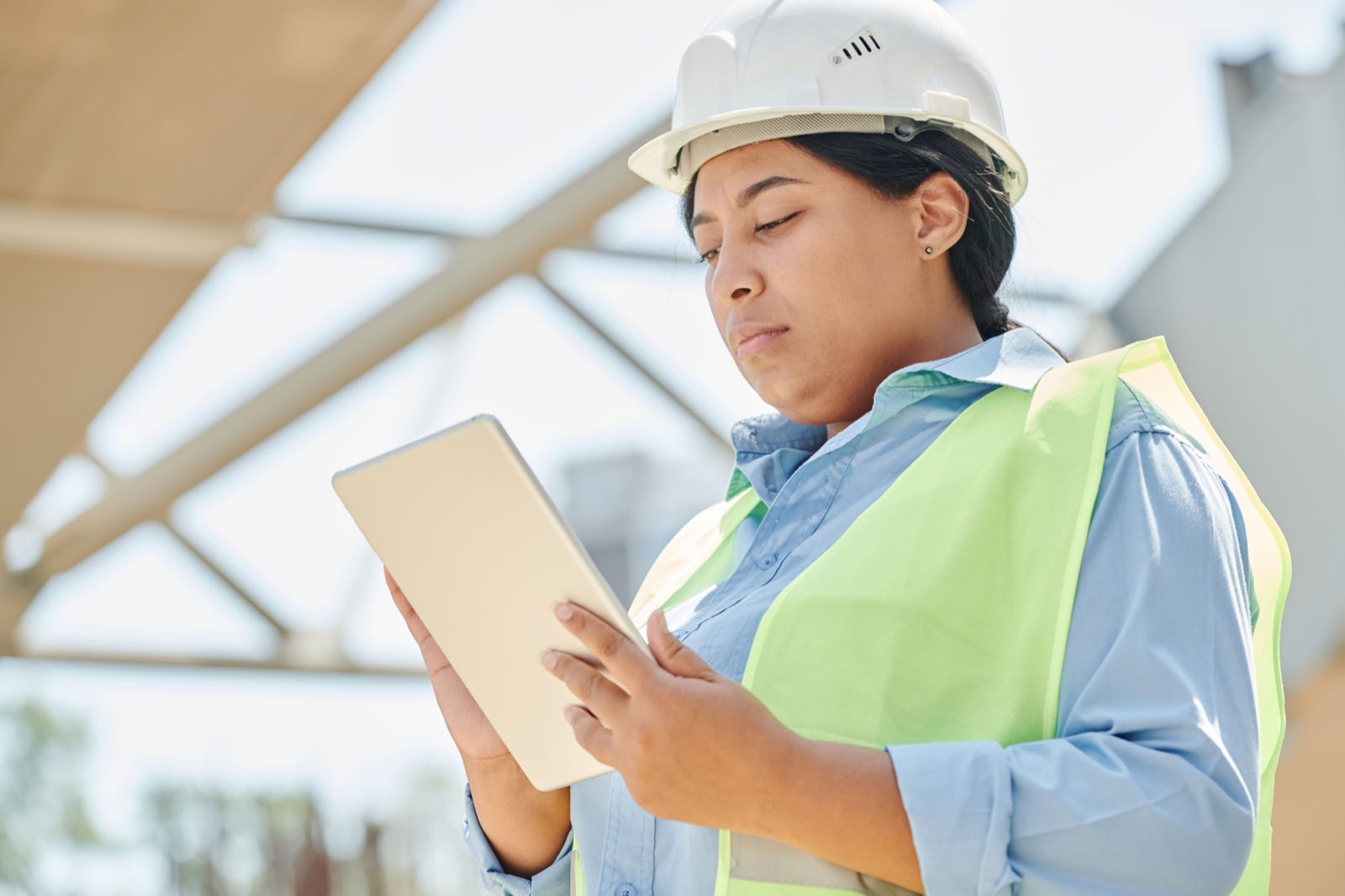 A facility engineer in a hard hat using a tablet on a manufacturing floor