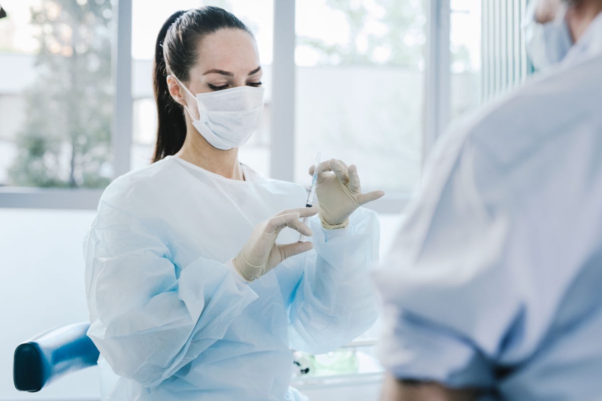 A doctor in protective gear preparing a syringe in a medical setting