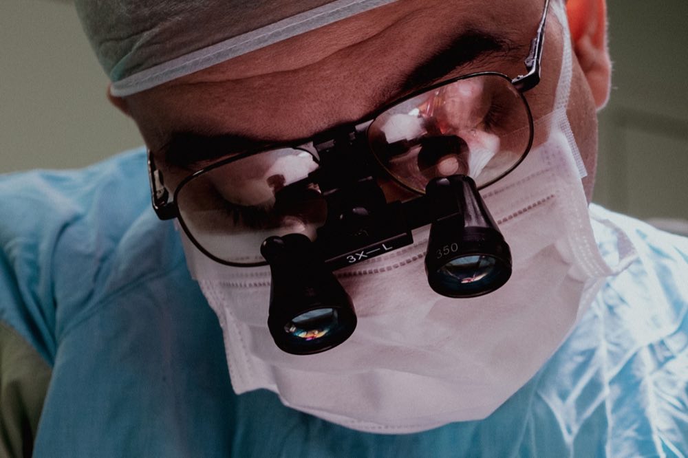 Close-up of a surgeon wearing surgical mask and loupes, demonstrating focus and expertise in medical procedure