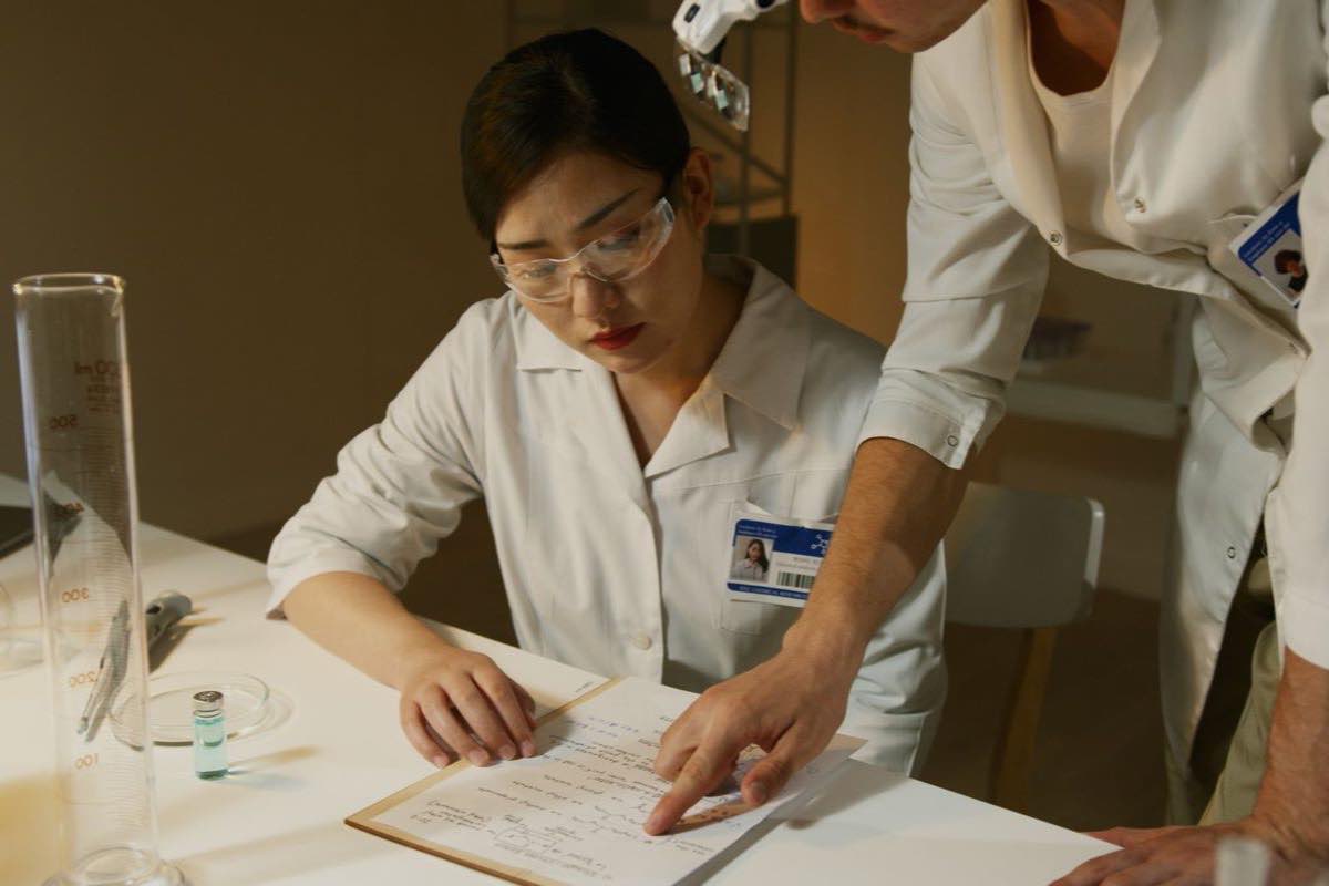 Two researchers in lab coats reviewing a controlled document binder
