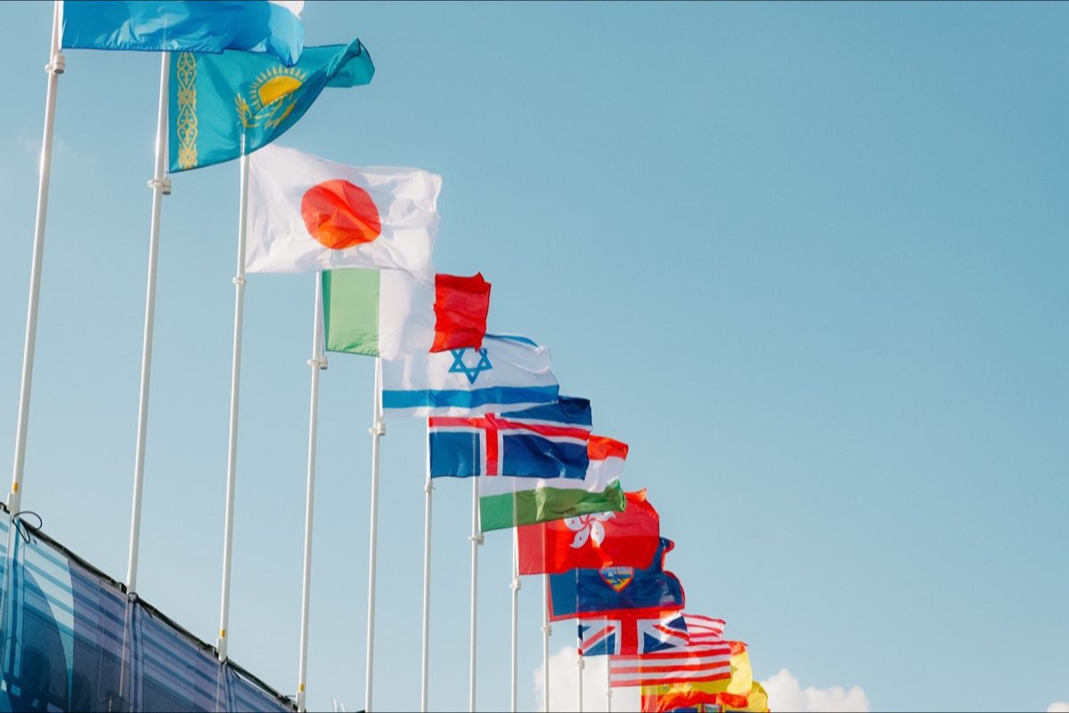 A line of international flags receding in sequence against a clear sky