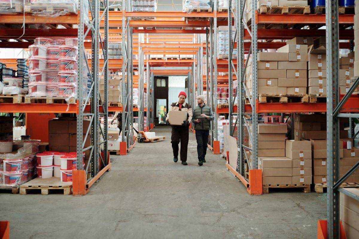 Warehouse workers handling a package among stocked shelves