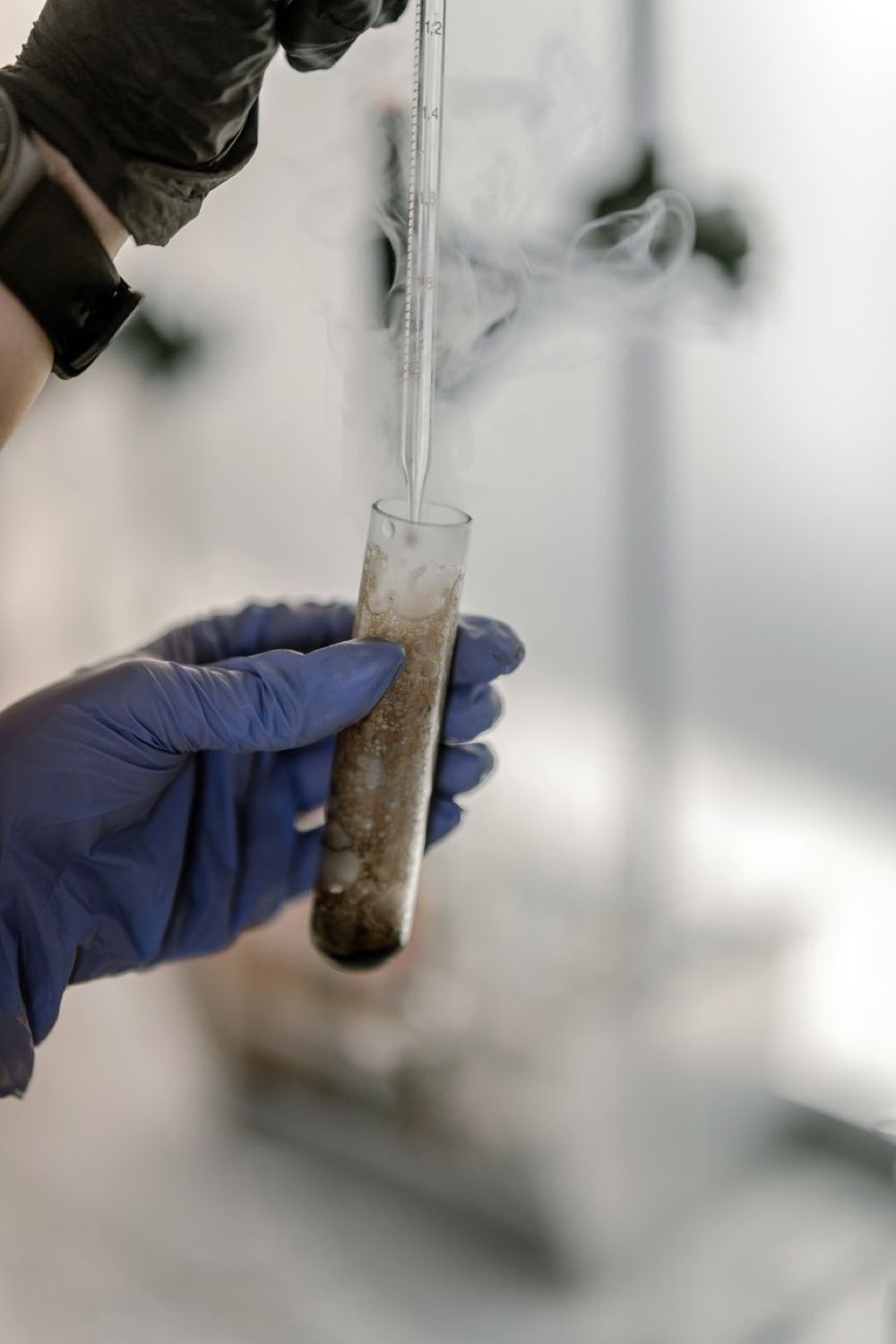 Gloved hands holding a vapor-shrouded cryogenic sample tube