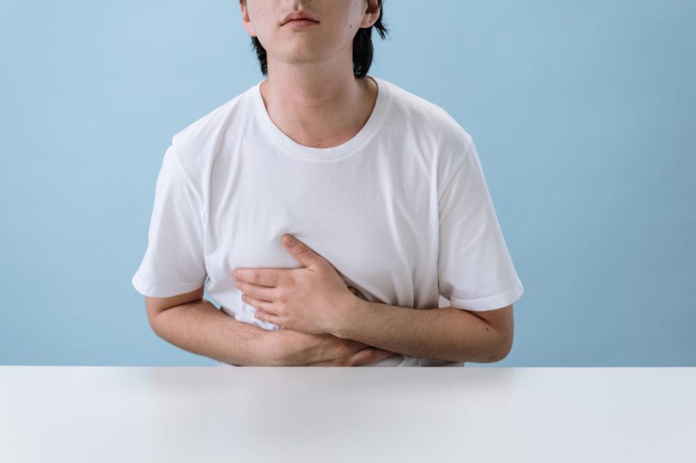 An adult man in a white shirt holds his stomach, indicating pain and discomfort, with a light blue background