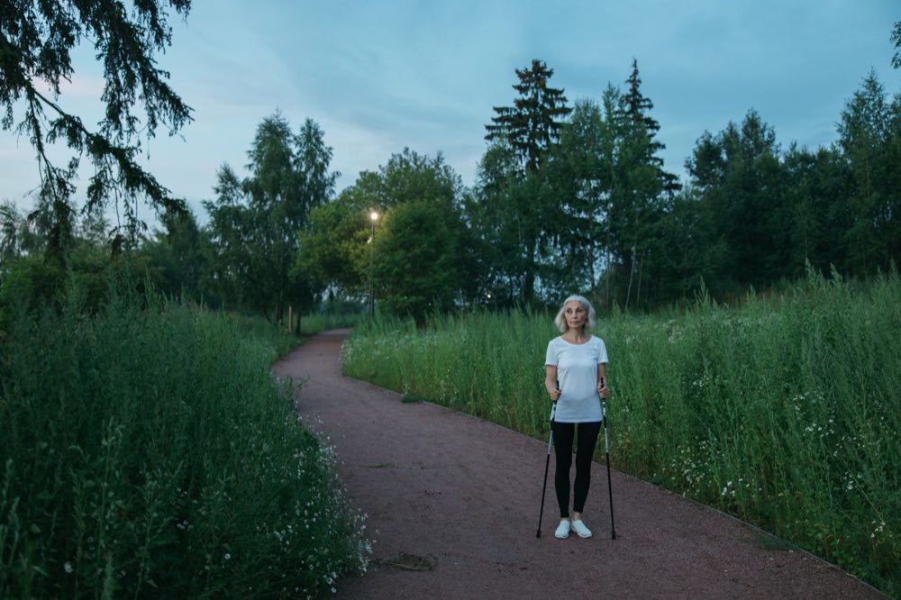 Senior woman exercising with Nordic walking poles in a peaceful green park during daytime