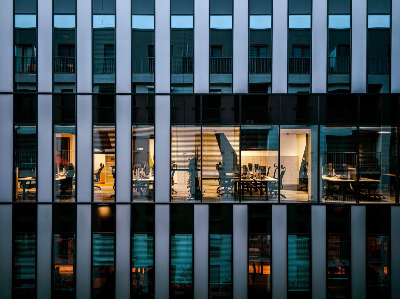 A modern office tower at dusk, its meeting rooms lit from within