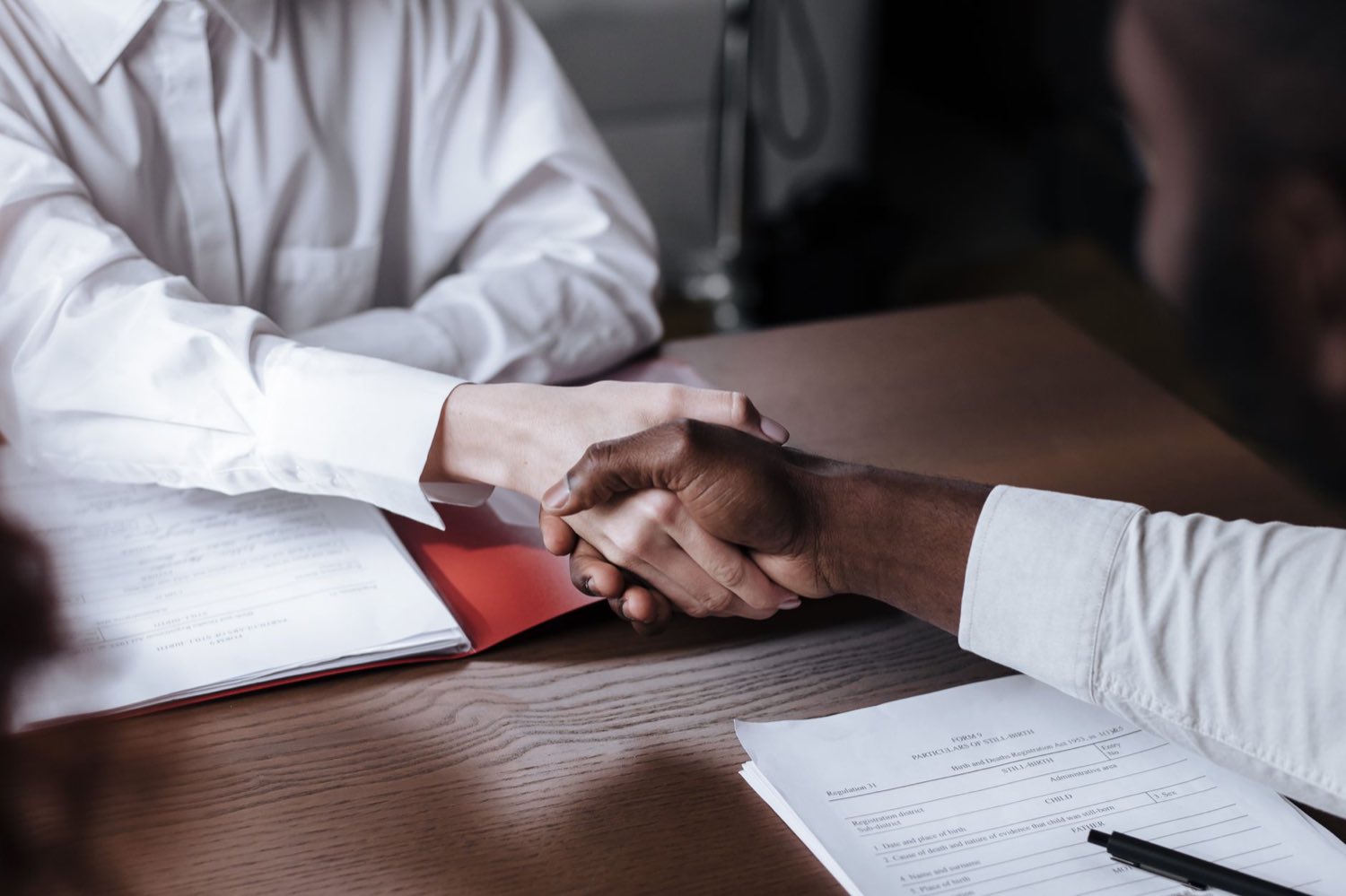 Two senior professionals shaking hands over a signed agreement