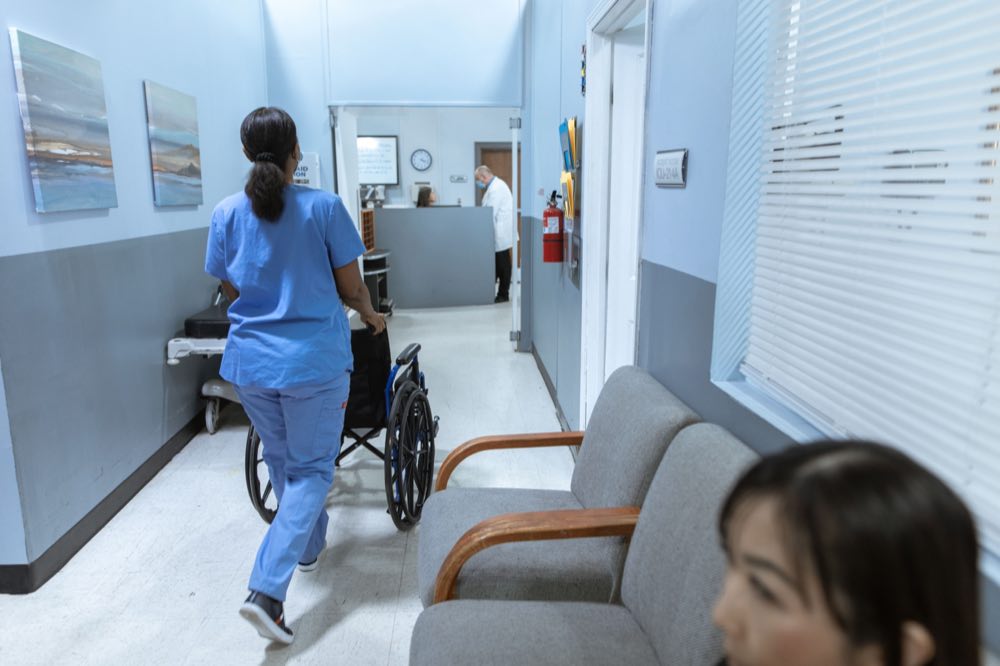 A nurse moving a wheelchair through a bright hospital corridor