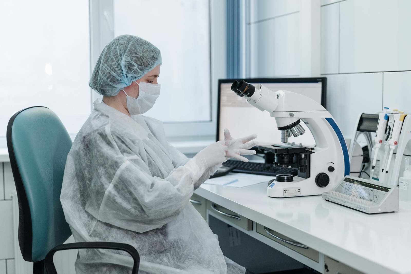 A scientist in protective gear examining samples under a microscope