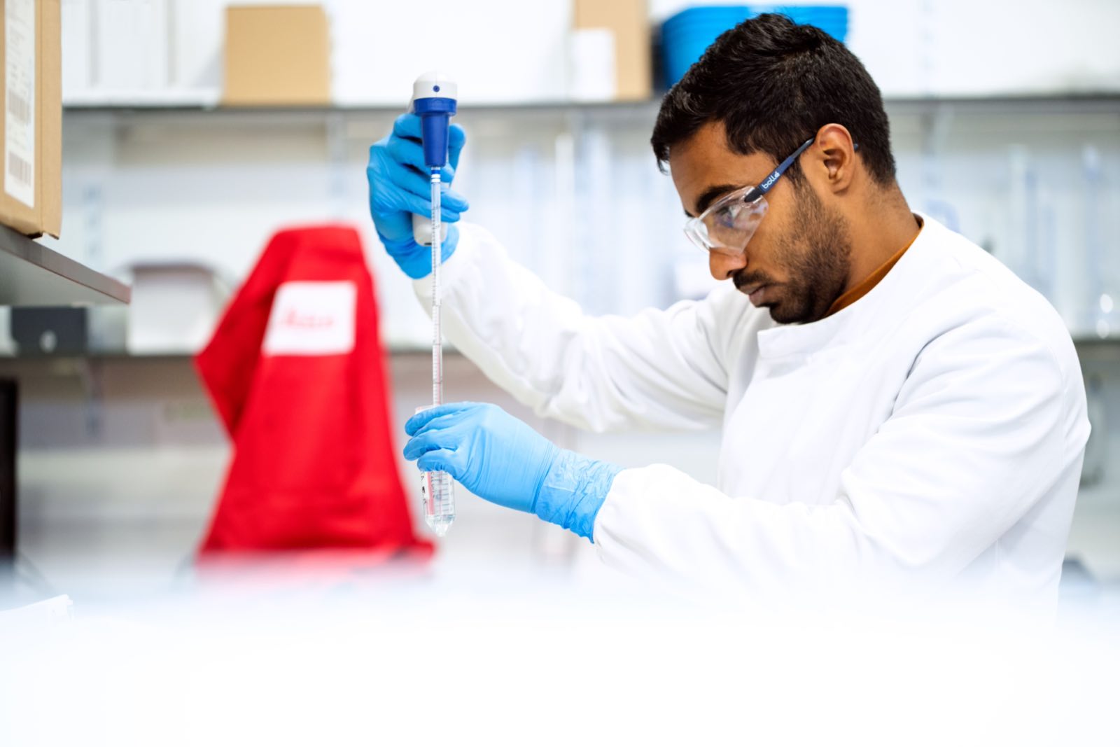 A scientist in safety glasses drawing up a sample with a pipette at a laboratory bench