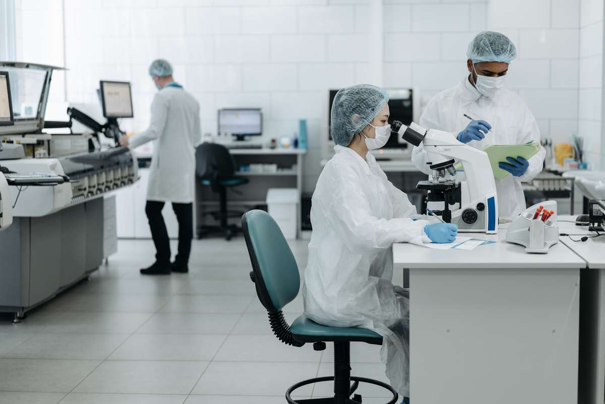 Scientists in gowning examining samples at a microscope in a regulated laboratory