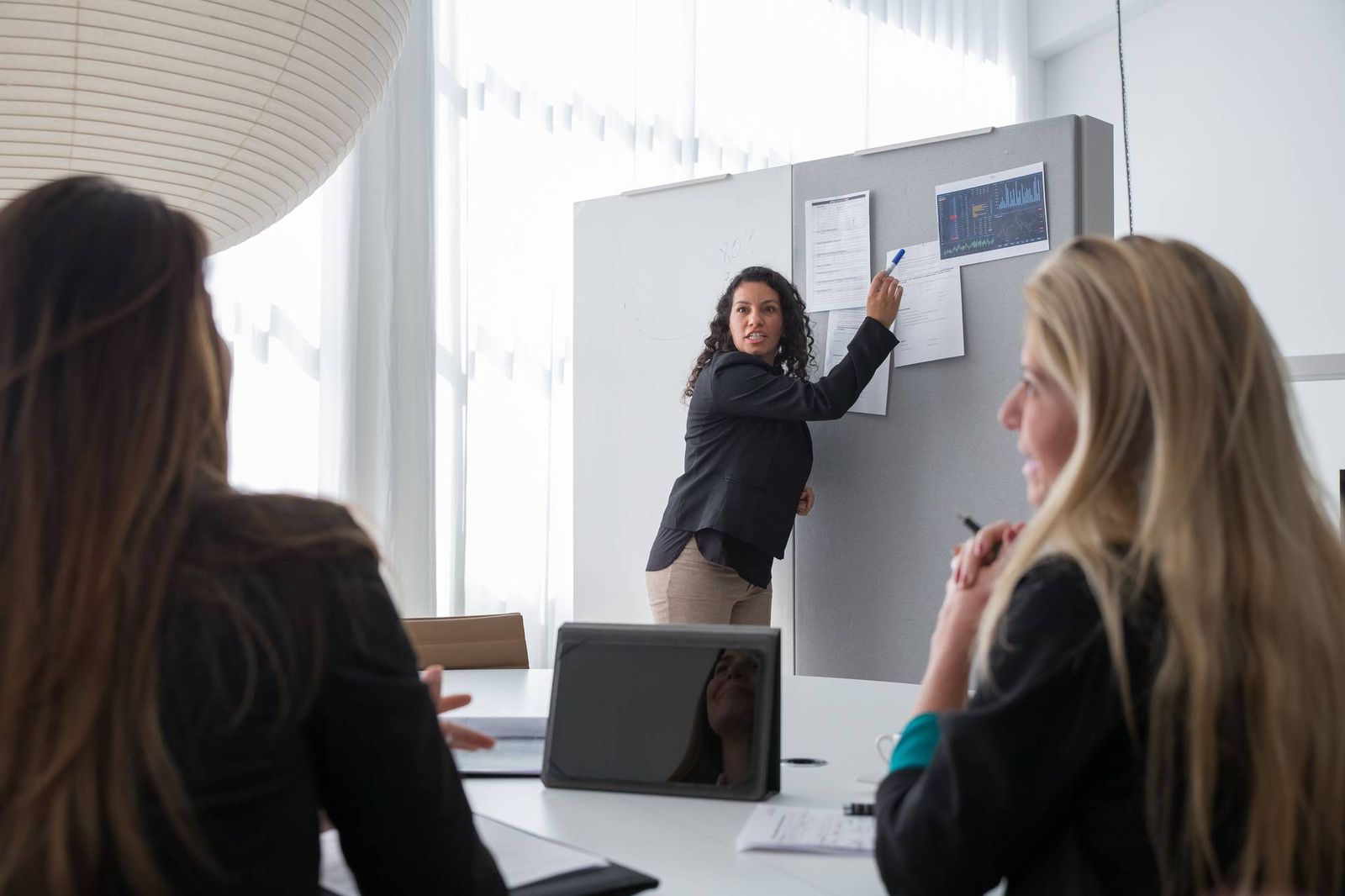 A presenter reviews trial-timeline charts on a flip chart with two colleagues seated at a conference table