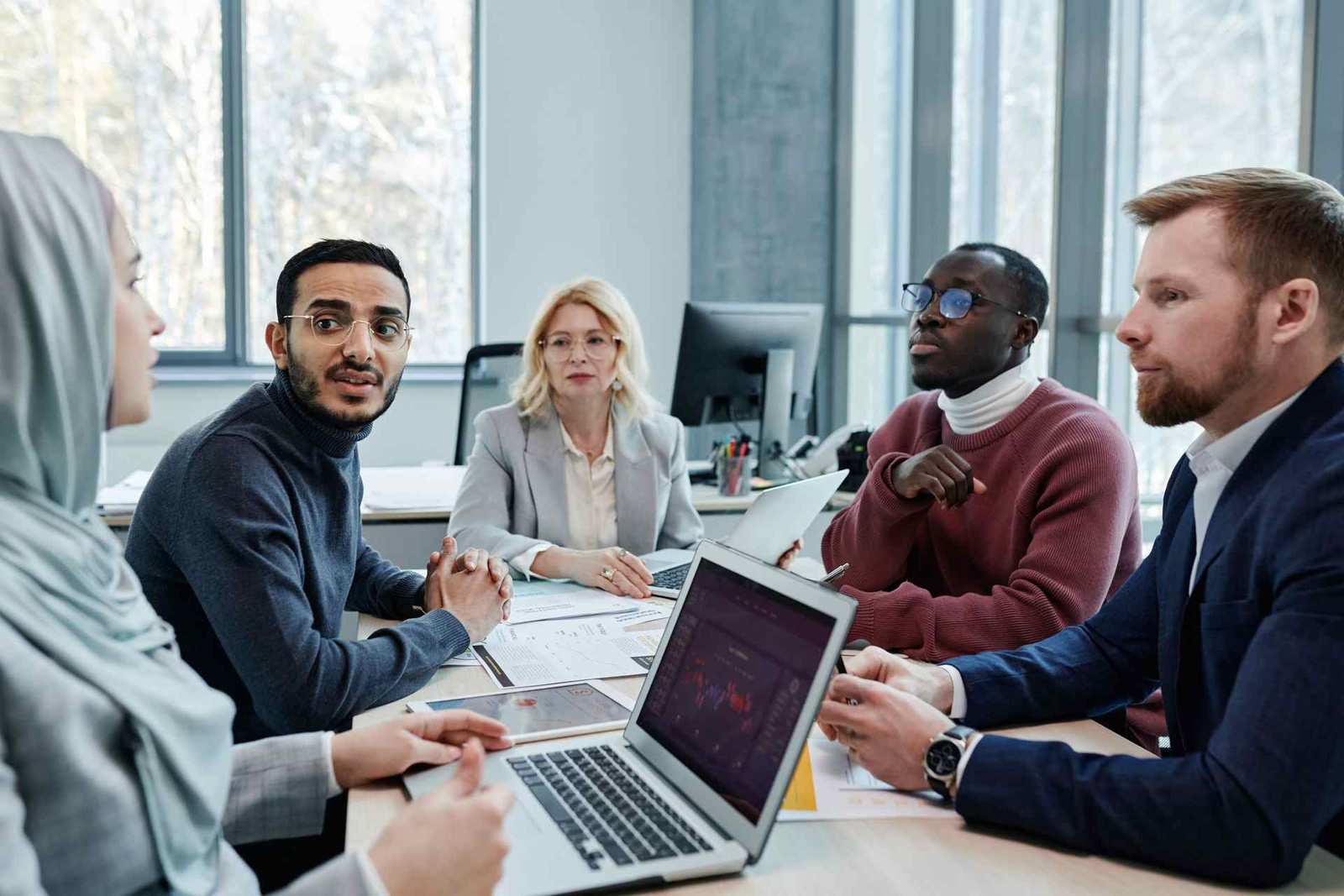 Five colleagues in a bright conference room discussing documents and a laptop together