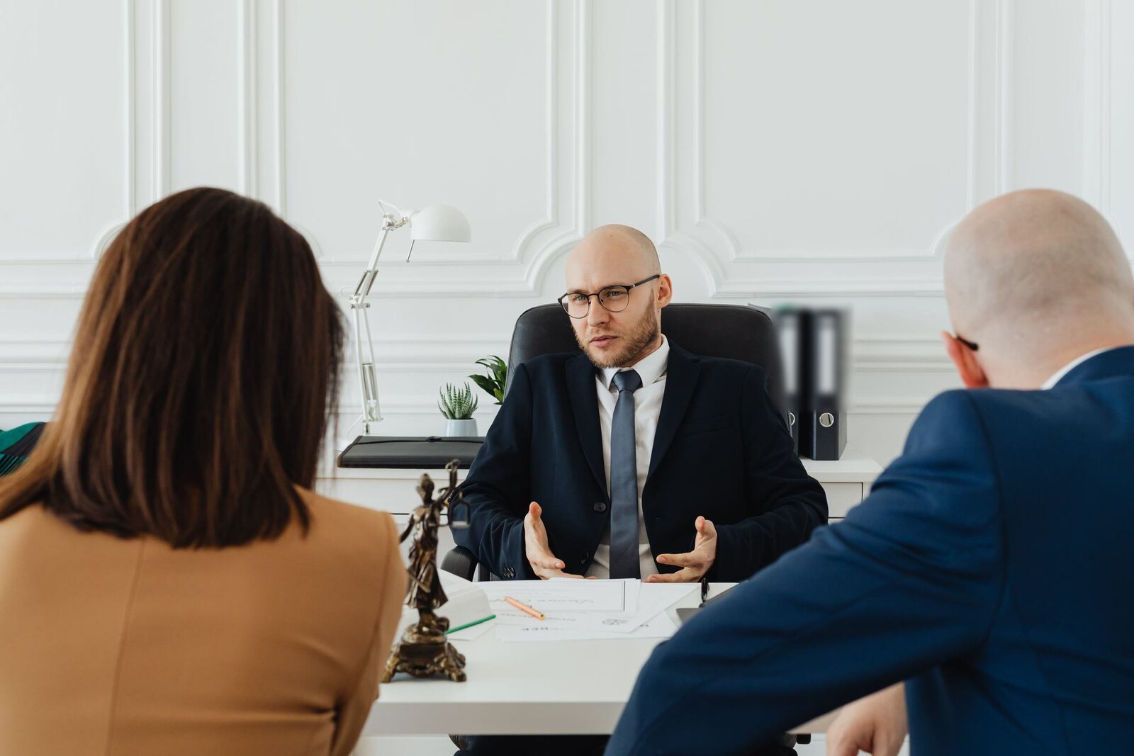 Regulatory advisor in a navy suit explaining a document across a white desk to two colleagues in a bright office