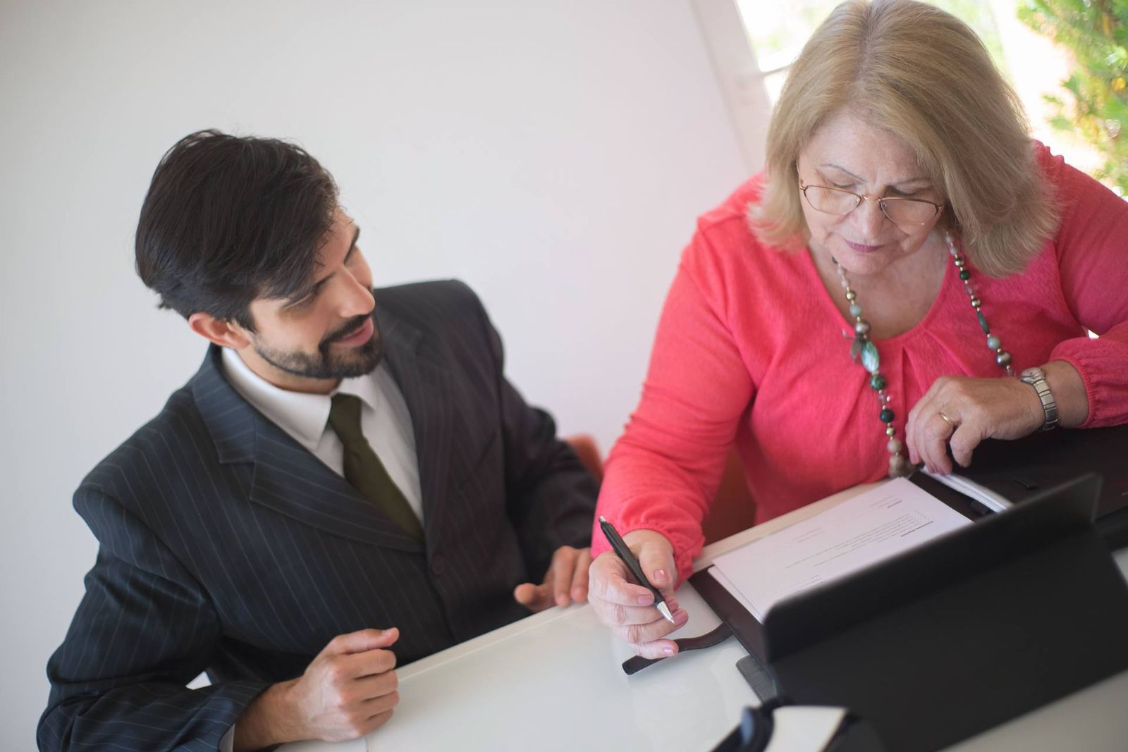 A pinstripe-suited advisor and a client in pink reviewing and signing a document together