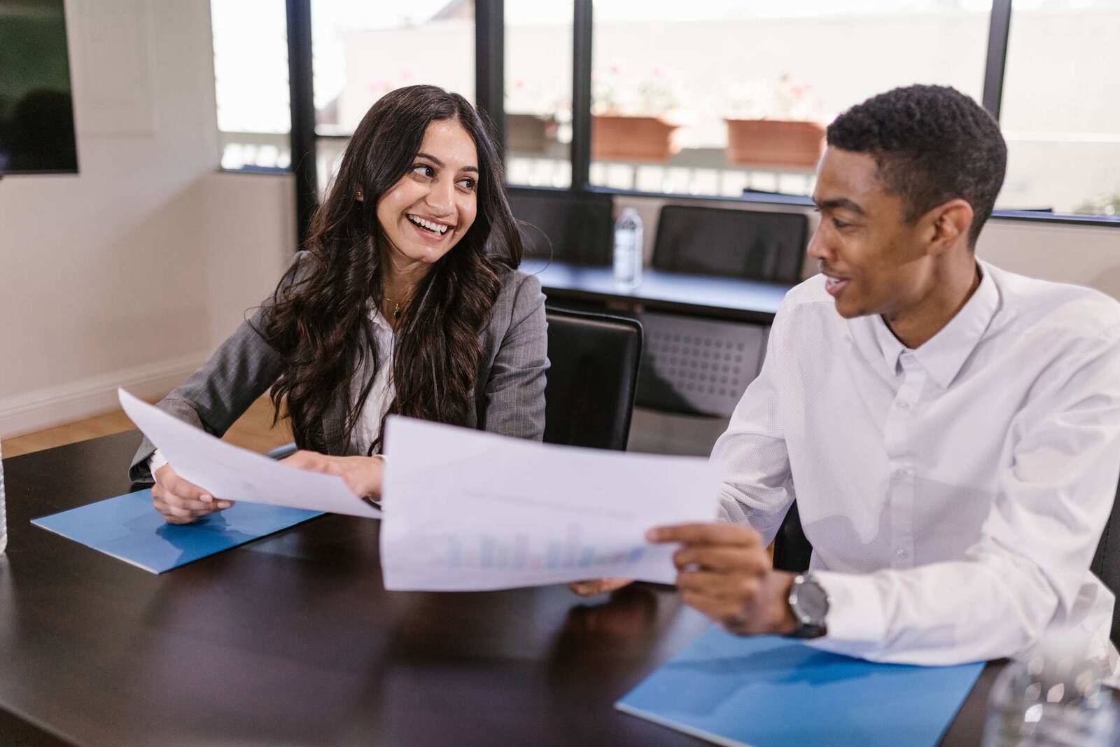 Two regulatory colleagues smiling while reviewing a printed chart document at a boardroom table