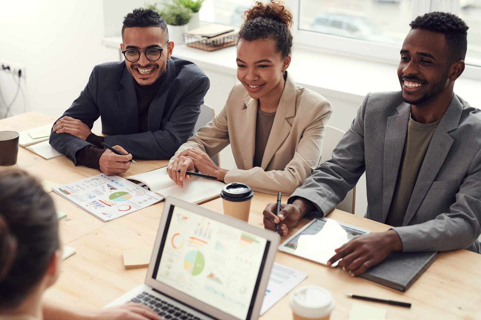 Three colleagues smiling while reviewing printed charts and a laptop dashboard around a table