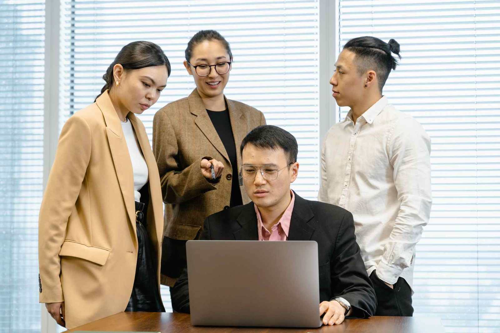 Four colleagues gathered around a laptop reviewing analysis on screen in a bright conference room
