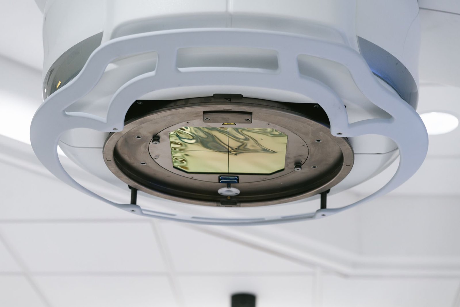 A ceiling-mounted surgical imaging device with a gold detector panel in a modern operating theatre