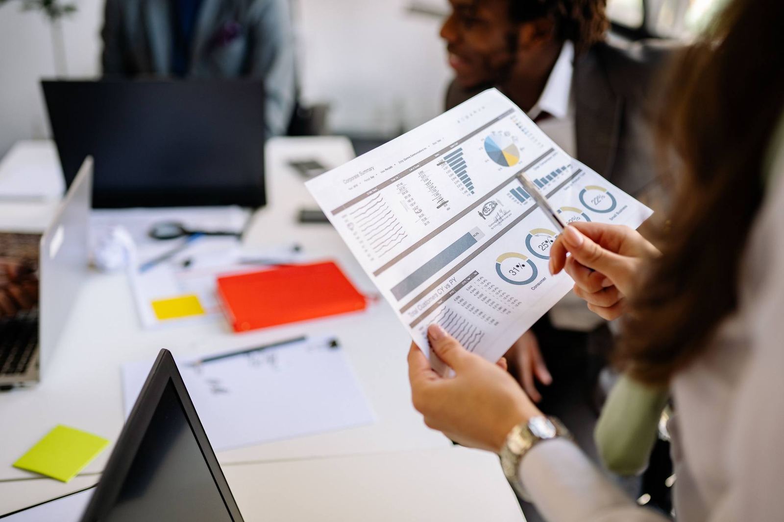 Two colleagues reviewing a printed data report with pie charts and percentage figures in a bright office