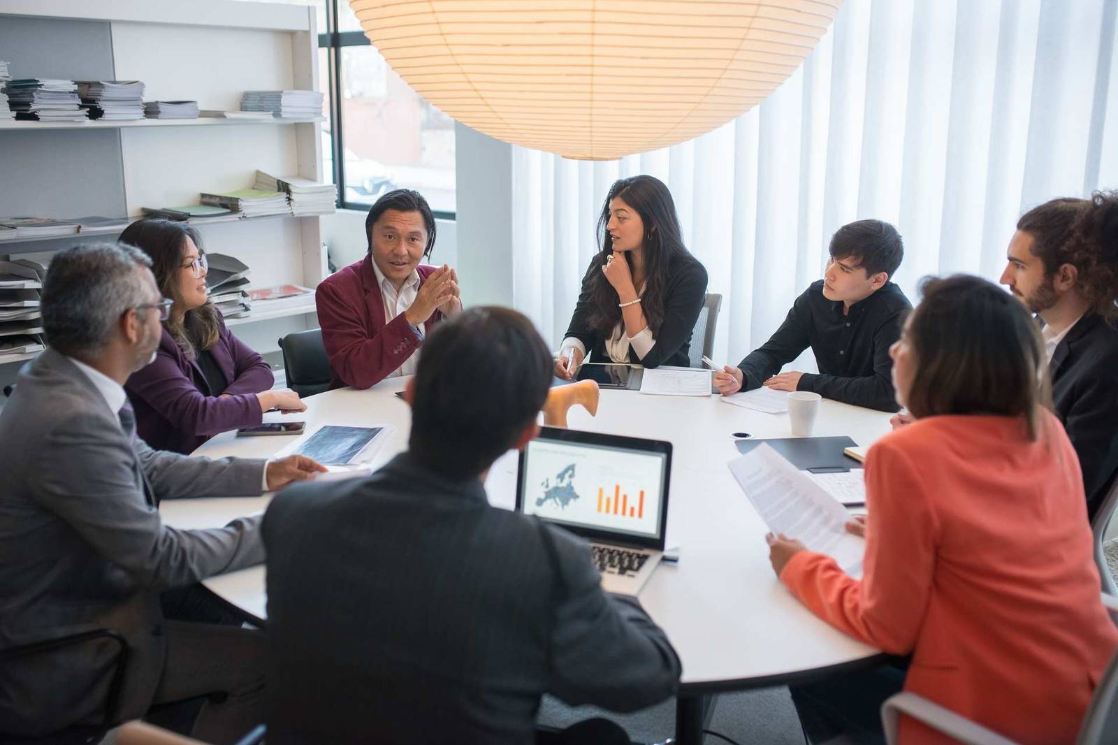 A diverse team of regulatory professionals in discussion around a conference table, with a laptop showing a Europe map and chart