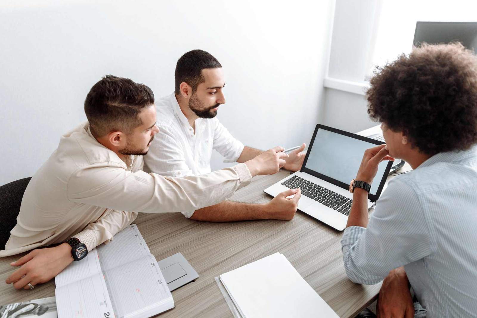 Three colleagues in business attire review a document and a laptop together in a bright office