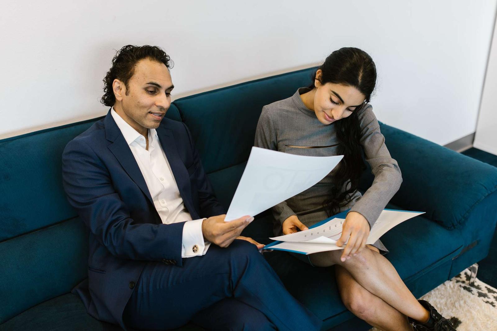 Two colleagues seated on an office sofa reviewing a printed study document together