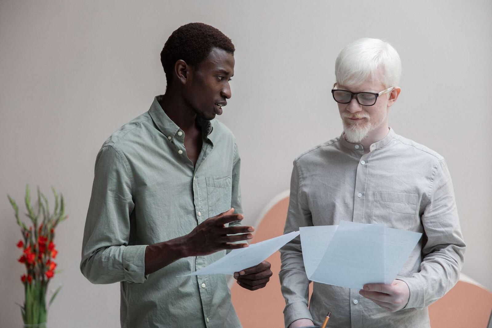 Two colleagues discussing printed documents while standing in a bright office